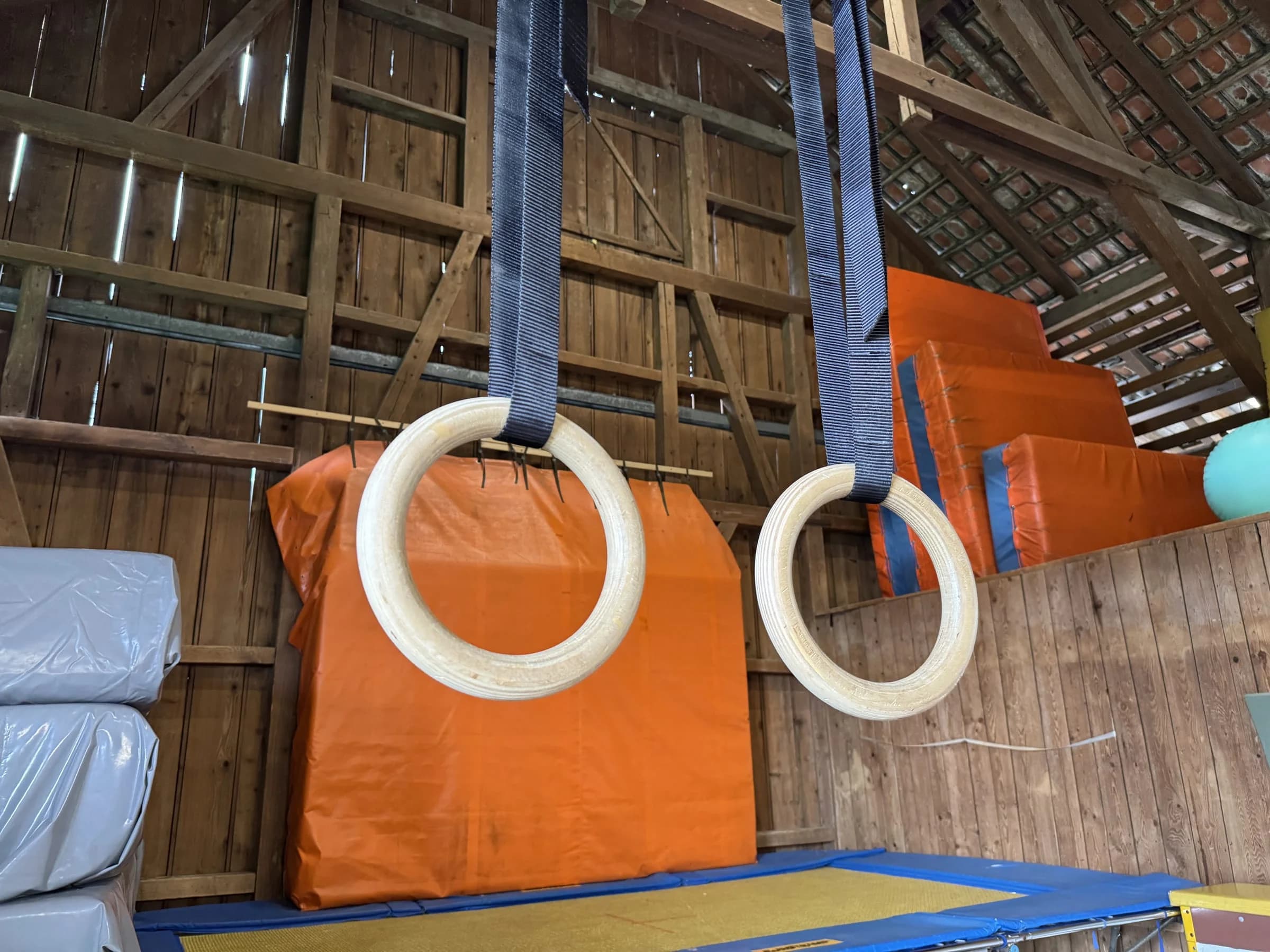 Zwei Holzringe an blauen Bändern über einer orangen Weichbodenmatte