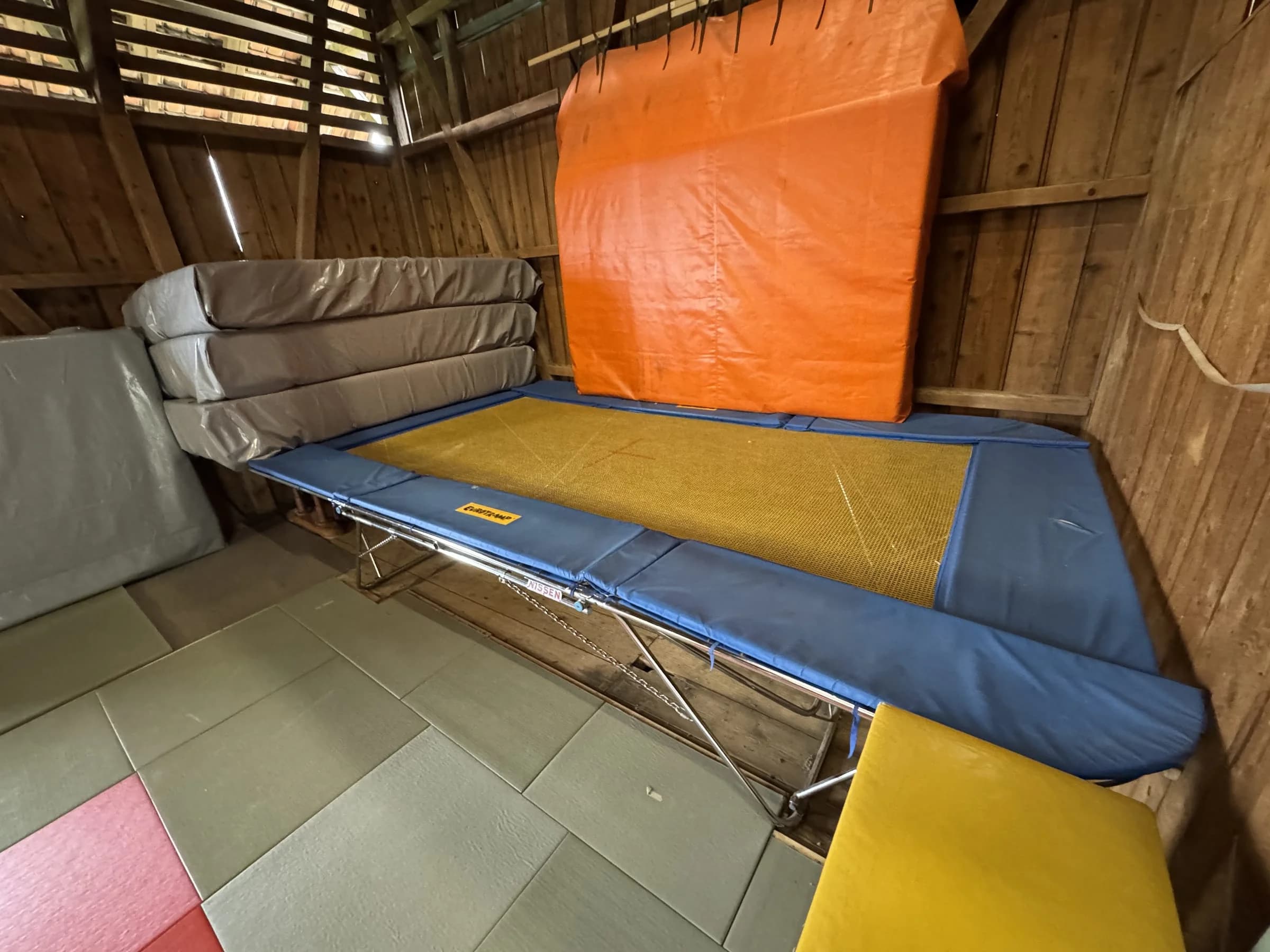 Grosses Trampolin unter dem Scheunendach, daneben gestapelte Weichböden